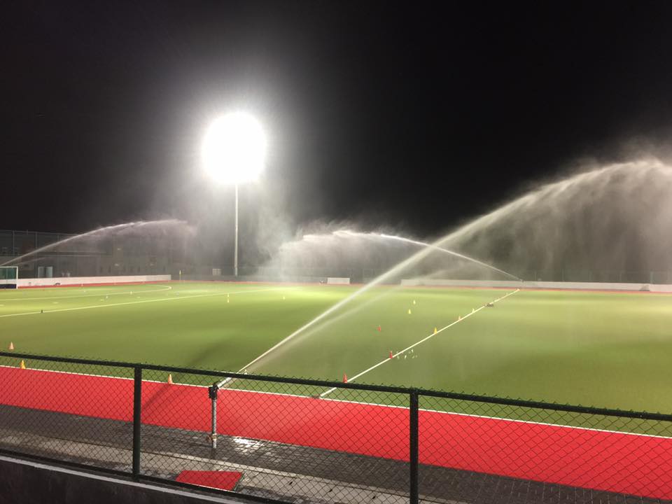 Night view of a sports field with bright floodlights and sprinklers watering the artificial turf, ensuring optimal conditions for gameplay with perrot distributor nanotech